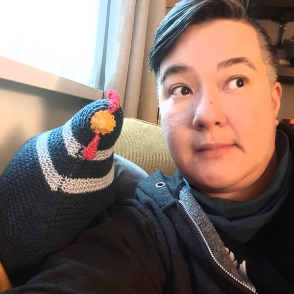 I am looking off camera at the TV, and a navy blue knitted chicken is leaning against my shoulder, it looks like we're discussing the TV programme.