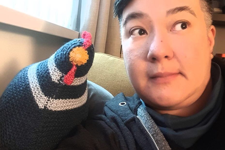I am looking off camera at the TV, and a navy blue knitted chicken is leaning against my shoulder, it looks like we're discussing the TV programme.