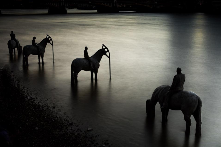 Four concrete statues of horses and riders stand in the water near the bank. The heads of the horses are the "nodding donkey" shapes of oil well pumps. They are positioned to look like they have come down to the water to drink.