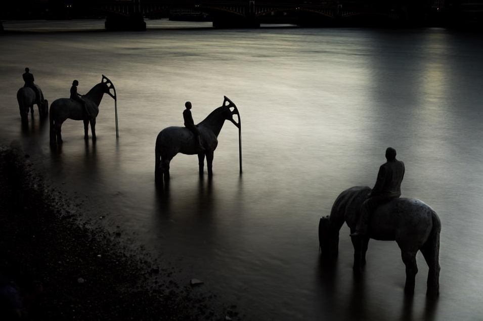 Four concrete statues of horses and riders stand in the water near the bank. The heads of the horses are the "nodding donkey" shapes of oil well pumps. They are positioned to look like they have come down to the water to drink.