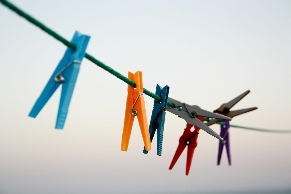 A green clothes line with coloured plastic pegs, on a grey background.
