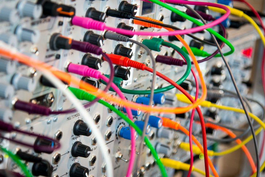 Lots of different coloured cables and jacks plugged into an electronics board with dials and knobs. It looks complex (but it might just be complicated!)