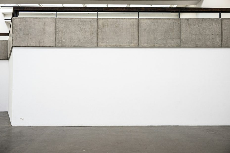 A white wall topped with concrete blocks and a black railing, under skylights.