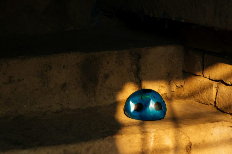 A blue plastic half-deflated football sits on a step in a ray of sunshine.