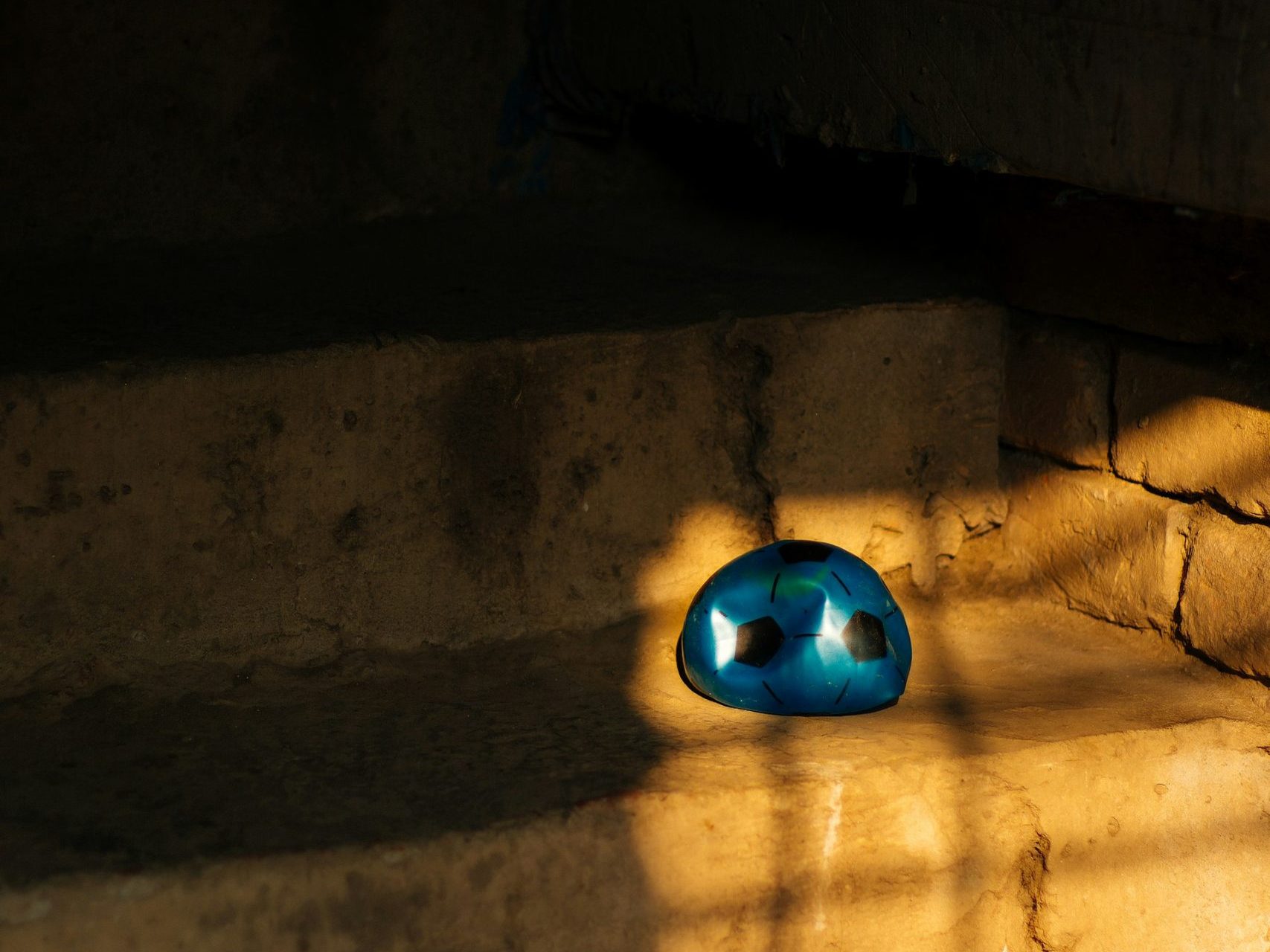 A blue plastic half-deflated football sits on a step in a ray of sunshine.