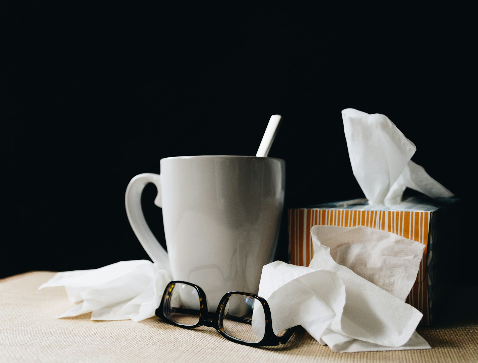 A mug and glasses next to a box of tissues.