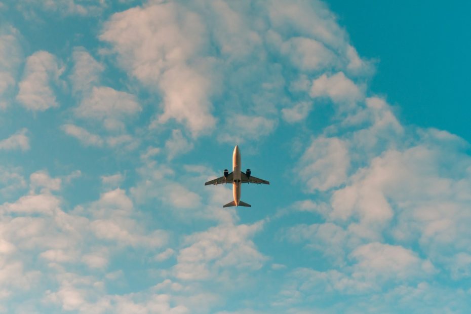 An airplane seen from below, against a blue sky and fluffy clouds.