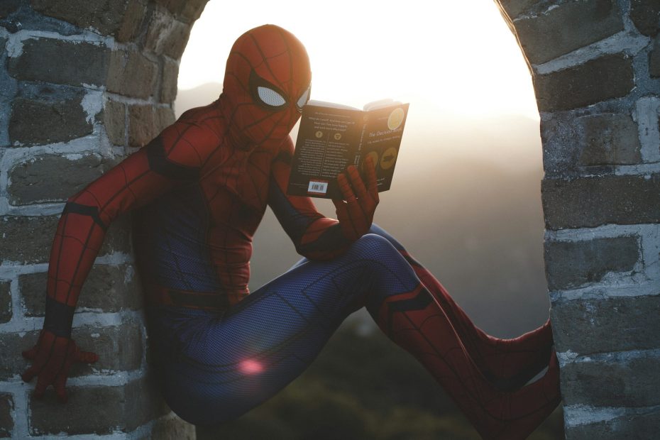 Spiderman is wedged in a stone archway, reading a book.