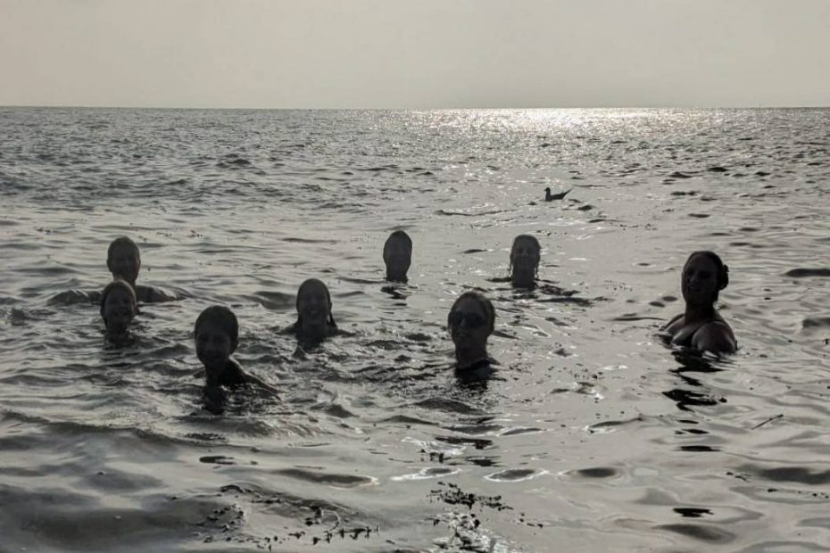 8 people bobbing in the sea, all you can see are smiley heads, and a couple of seagulls bobbing a bit further away.