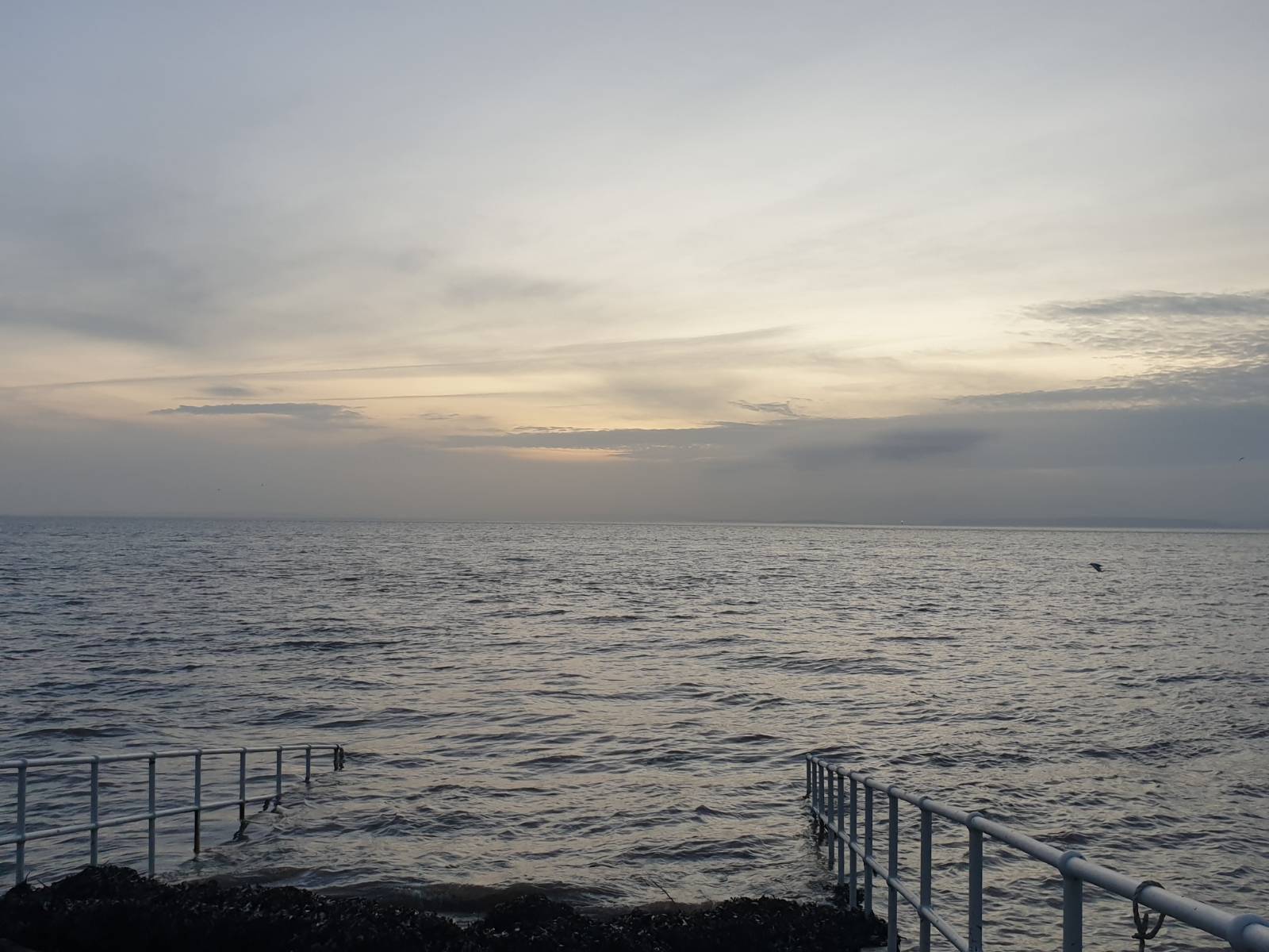 The sea at Penarth at high tide at dawn, looking south from the RNLI lifeboat station. There's cloud cover on the horizon and the dawn light above that.