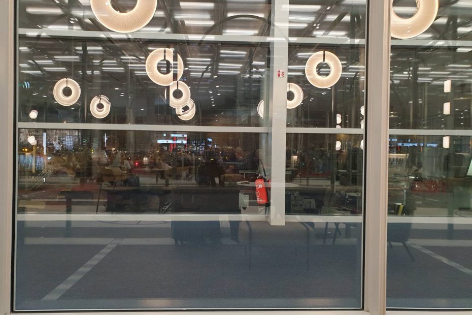 It's dark outside and the photo captures the reflections in the airport bay windows of the lights shaped like doughnuts and the seats inside the passenger lounge.