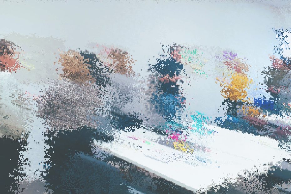 A pixelated image of a group of people standing around talking, in a workshop setting.