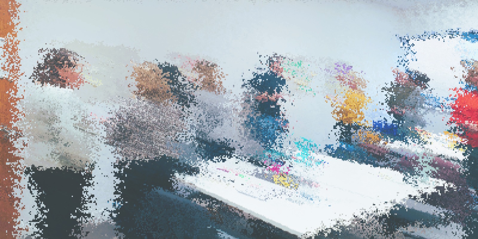 A pixelated image of a group of people standing around talking, in a workshop setting.