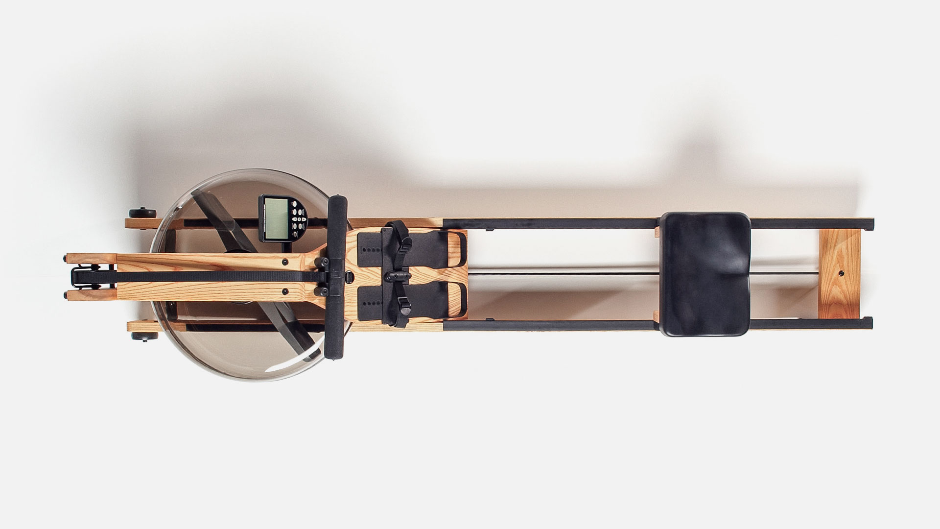 A water rower seen from above. It's basically a rowing machine which has a big round tank of water at the front, with a paddle which spins when you pull the handles and cord. The faster you pull, the stronger the water resistance. Your feet strap in near the water tank, and the seat slides along two wooden rails. It's about 2 meters long in total. It's built out of wood mostly, with black accents for the handle and cord, the adjustable footrests, and the seat. It is visually very pleasing.